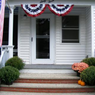 A front porch adorned with patriotic bunting and seasonal decorations, including pumpkins and flowers.