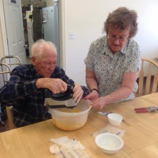 An elderly couple enjoys baking together in the kitchen.
