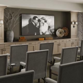 A cozy home theater setup with rows of chairs facing a large screen displaying a black and white movie.