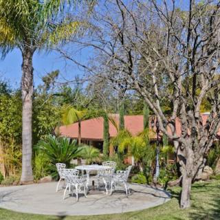 A tranquil garden setting with a patio area featuring outdoor furniture surrounded by lush trees and greenery.