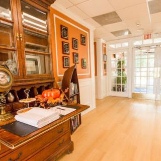 A warmly decorated hallway with a vintage wooden desk and framed pictures on an orange wall.