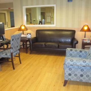 A cozy living area featuring a leather sofa, patterned chairs, and a computer desk, illuminated by warm lamps.