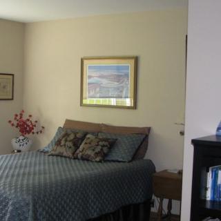 A cozy bedroom with a neatly made bed, decorative pillows, and artwork on the wall.