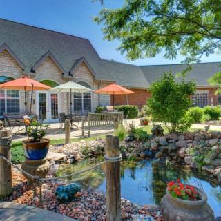 A tranquil garden with a pond, surrounded by patio seating and colorful umbrellas.