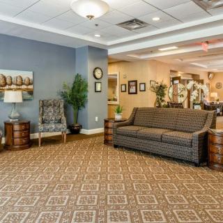 A cozy lobby area featuring a patterned carpet, sofa, chairs, wall art, and indoor plants.