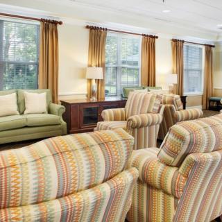 A cozy living room with striped armchairs and a green sofa, accented by warm lighting and large windows.