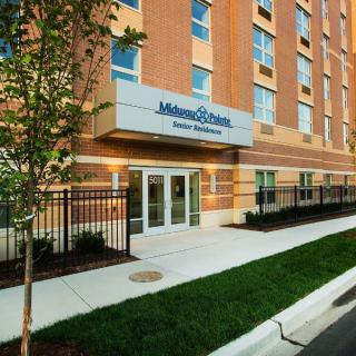 The entrance of a modern brick building with trees and a sidewalk in front.