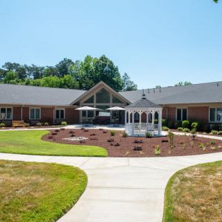A residential building with a landscaped garden and a central gazebo, surrounded by a pathway on a clear day.