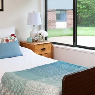 A cozy bedroom with a single bed, bedside table, and large window offering plenty of natural light.