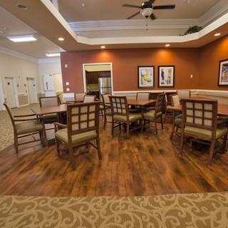 A cozy dining area with wooden flooring, tables and chairs, and warm lighting.