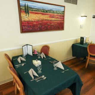 A cozy dining area with neatly set tables and a landscape painting on the wall.