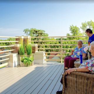 A group of seniors sitting and enjoying the view on a sunny deck surrounded by greenery.