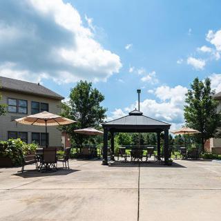 A sunny outdoor patio with a gazebo, surrounded by chairs and umbrellas near a building.