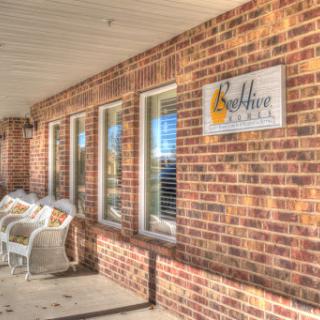A cozy brick building entrance featuring a welcoming sign and outdoor seating.