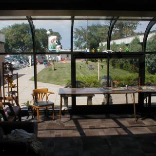 A brightly lit indoor space with large windows overlooking a garden, featuring tables and chairs arranged in the sunlight.