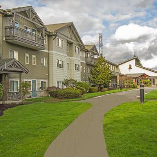 A residential apartment building with a well-maintained lawn and pathway under a cloudy sky.