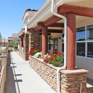 A modern building with stone columns, vibrant flowers, and an outdoor walkway on a sunny day.