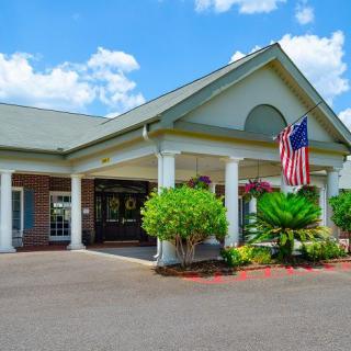 A well-maintained building entrance with an American flag, surrounded by greenery under a partly cloudy sky.