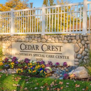 A stone sign for Cedar Crest, an Alzheimer's Special Care Center, surrounded by flowers and a white fence.