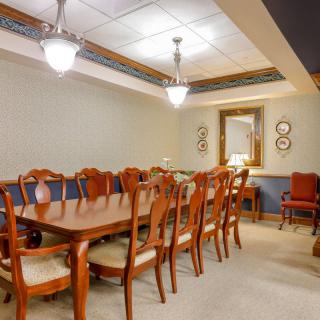 A well-lit dining or conference room with a large wooden table surrounded by chairs and a mirror on the wall.