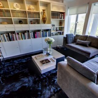 A modern living room with bookshelves, a comfortable sofa, and natural light from large windows.