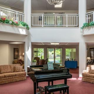 A spacious lobby area featuring a black grand piano, surrounded by comfortable sofas and adorned with indoor plants under a chandelier.