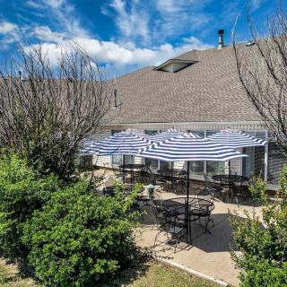 A sunny patio area with striped umbrellas, tables, and chairs surrounded by greenery.