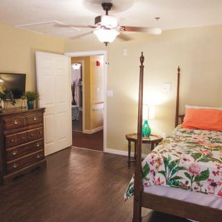 A cozy bedroom featuring a four-poster bed with floral bedding, a wooden dresser, and a side table with a lamp.