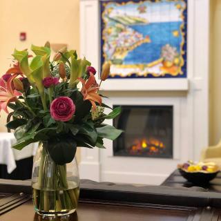 A cozy interior featuring a vibrant flower arrangement in a vase next to a lit fireplace, with colorful artwork on the wall.