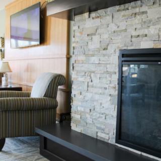 A cozy living room featuring a stone fireplace, armchair, and a mounted television.