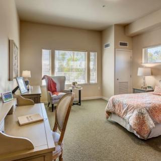 A cozy bedroom with a bed, desk, and large windows letting in natural light.