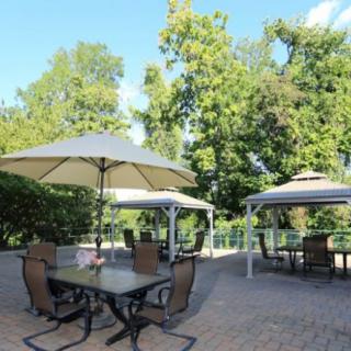 A cozy outdoor patio with tables, chairs, and umbrellas surrounded by lush greenery.