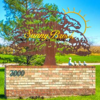 A decorative sign in a park setting, featuring a tree silhouette and the text 'Sunny Bunn' above a brick wall.