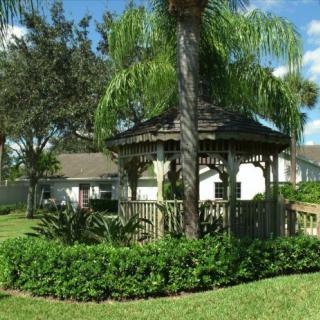 A charming gazebo surrounded by lush greenery and palm trees in a residential garden.