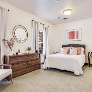 A cozy and well-decorated bedroom featuring a bed with decorative pillows, a wooden dresser with a circular mirror above, and soft lighting.