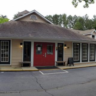 An exterior view of a restaurant with a prominent red door and large windows, set against a backdrop of greenery.