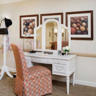 A well-arranged vanity desk with a mirror, stylish chair, and decorative artwork on the wall.