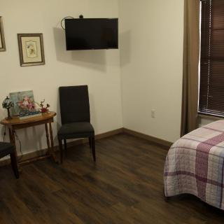 A cozy bedroom featuring a TV, chairs, and a neatly made bed on a wooden floor.