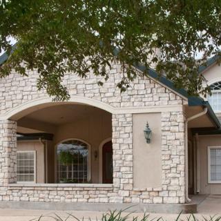 A charming house with a stone exterior and spacious porch, set under the shade of trees.