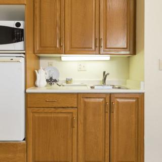A compact kitchen area with wooden cabinets, a sink, microwave, and refrigerator.