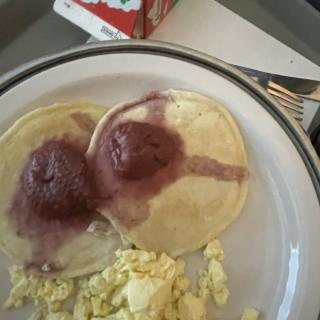 A breakfast plate with pancakes topped with syrup and scrambled eggs.