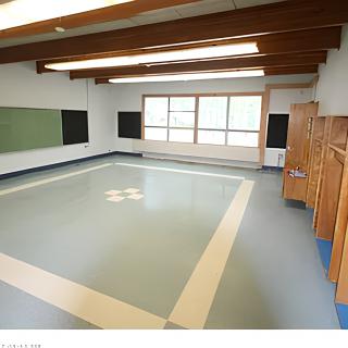 An empty classroom with wooden beams, large windows, and chalkboards.