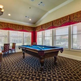 A well-lit game room featuring a pool table with large windows and decorative carpeting.
