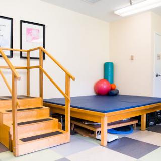 A well-equipped therapy room featuring a set of stairs, exercise mat, and fitness balls.