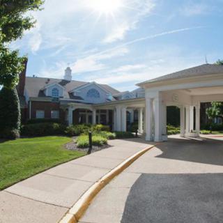 A large residential building with a covered driveway and manicured landscaping under a blue sky.