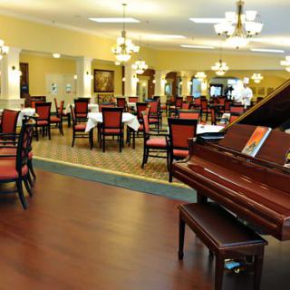An elegant dining area featuring a grand piano and neatly arranged tables with chairs.