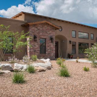 A modern house with a stone facade and desert landscaping under a blue sky with clouds.
