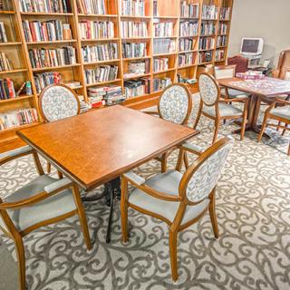A cozy library room featuring wooden tables surrounded by chairs and lined with bookshelves.