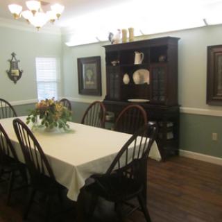 A formal dining room with a long table, chairs, and a wooden cabinet against the wall.