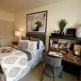 A cozy and well-decorated bedroom featuring a bed with patterned bedding, a desk with various items and a plant, stylish decor, and soft lighting.